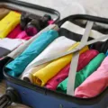 Ilustrasi tips packing liburan singkat dengan baju tergulung rapi dalam koper