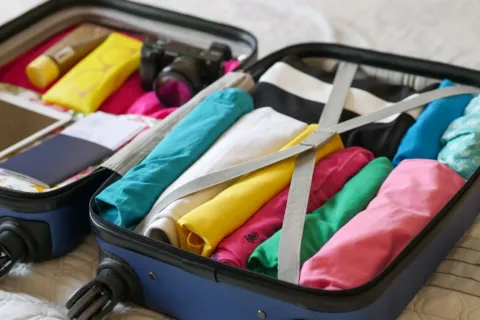 Ilustrasi tips packing liburan singkat dengan baju tergulung rapi dalam koper